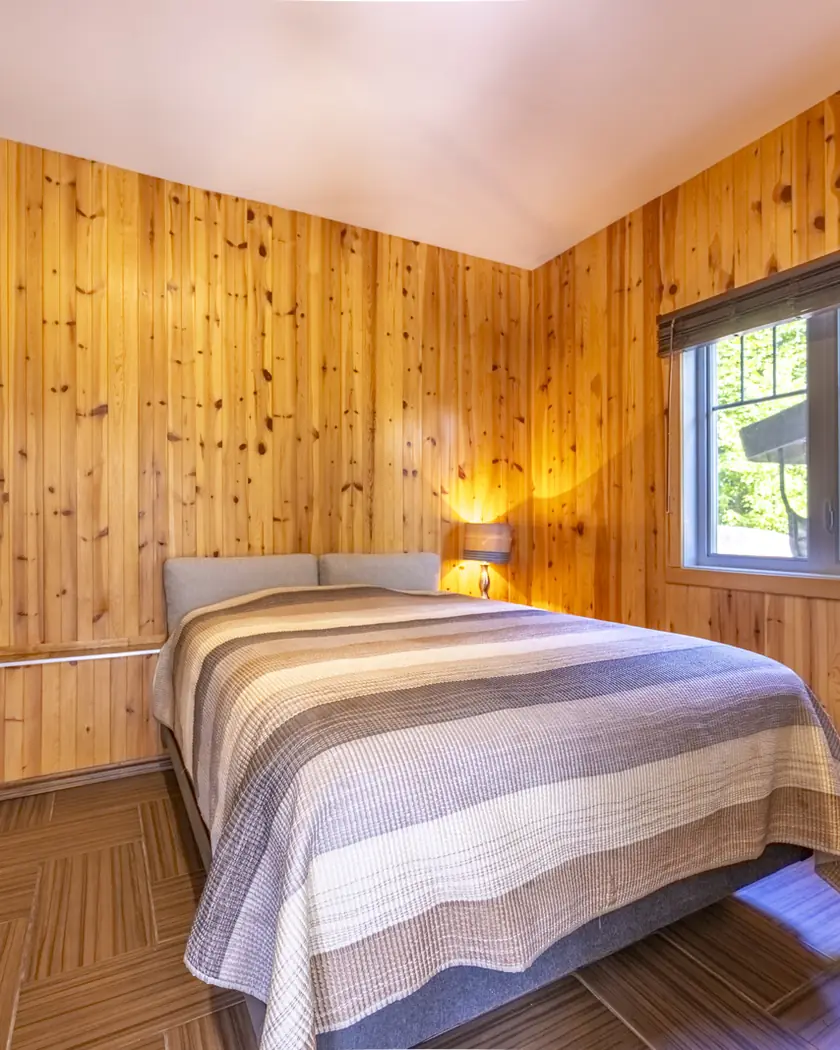 Chambre lambrissée de pin avec fenêtre donnant sur la forêt